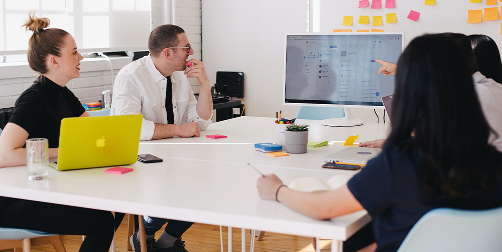 People sat around table looking at computer screen with findings from a rebranding workshop