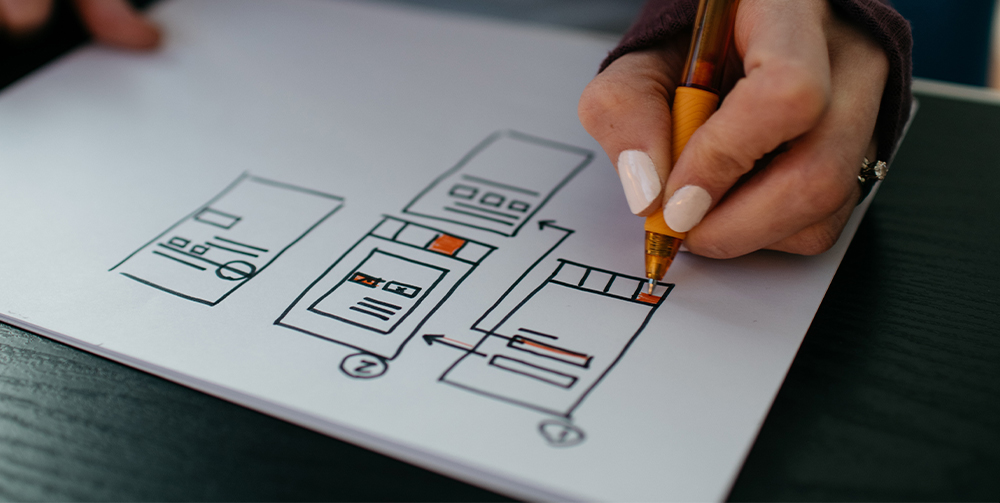 Close-up of a woman's hand sketching out a process using a pen on a pad